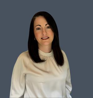 A picture of Ema Cubitt the Autism Reviewer.  Long dark hair, wearing a white blouse standing in front of a blue background.